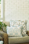 A wicker armchair with beige cushions and two pillows, including a Starfish Trio with Beach Lattice Lumbar Pillow for coastal charm, sits beside a green potted plant against a white brick wall.
