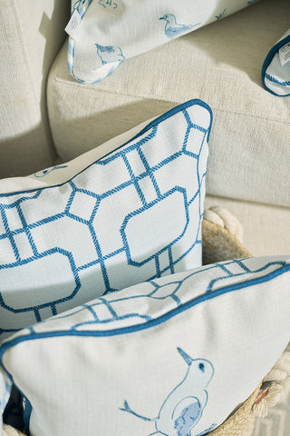 Two decorative pillows on a beige sofa: one with the Sewing Down South® blue geometric pattern, and another with blue birds. The Sandpiper Trio with Blue Lattice Lumbar Pillow enhances the beachy vibe in the background.