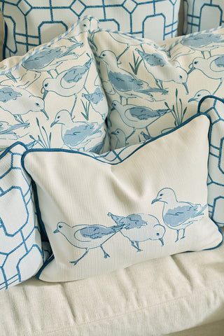 Four Sandpiper Pillows, featuring blue and white patterns—two with geometric designs and two showcasing a coastal seagull motif—are arranged on a light-colored sofa.