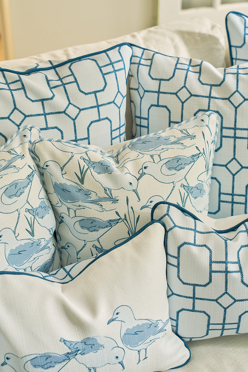 A close-up of decorative pillows with blue geometric patterns, featuring the Blue Lattice Oversized Pillow with a hand-drawn lattice design and coastal bird art, all arranged on a white couch with durable fabric.