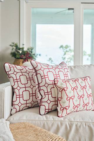 The Red Holiday Lattice Oversized Pillow and two other decorative pillows are arranged on a white sofa in a bright living room, adding festive charm as holiday pillow accents.
