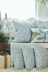 A cozy seating area features the Silver Bells Pillow along with white and blue twill woven pillows, all adorned with snowflakes and holiday motifs, set among festive greenery and soft, fluffy textures.