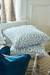 Two blue and white pillows with ice cream patterns are stacked on a textured surface near a window, accented by the Silver Bells Pillow and a twill woven pillow, with cone-shaped decorations nearby.