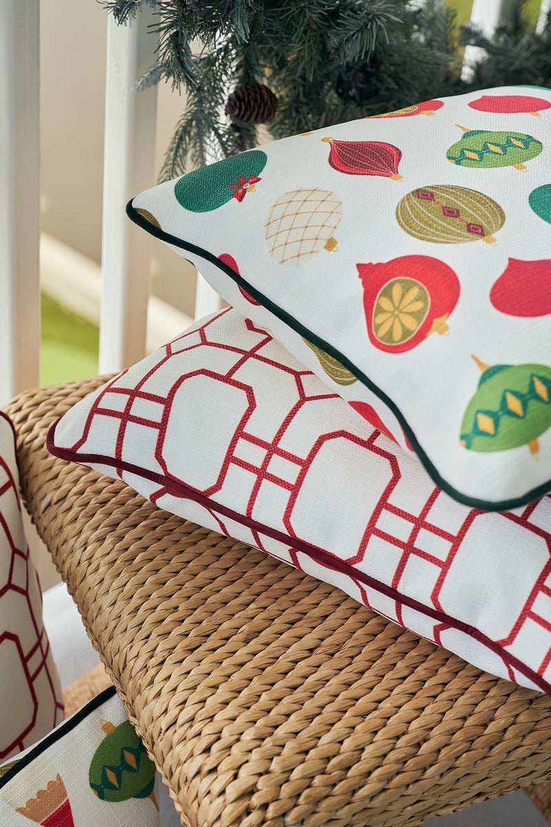 A Classic Ornaments Pillow with festive designs tops a red geometric pillow on a wicker chair, with pine branches and ornaments enhancing the holiday display.