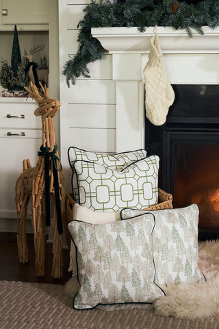 A cozy living room scene featuring the Green Holiday Lattice Oversized Pillow, patterned pillows, a woven basket, a cream knit stocking on a white fireplace, a plush rug, and a wooden reindeer by the hearth with greenery above the mantle.