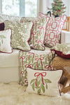 A white sofa holds the Jolly Holly Pillow, which features green and red mistletoe designs. Other pillows show geometric red patterns, and a small Christmas tree in the background completes the festive setting.