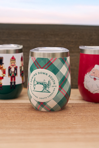 Three festive wine tumblers with different designs on a wooden surface.