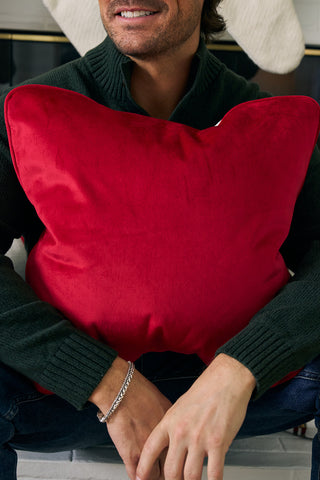 A person in a dark green sweater sits with the Nutcracker Stripe Pillow in Scarlet on their lap. Their face is partially visible, and they are smiling.