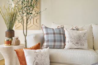 A cozy living room scene with a white couch, plaid pillow, patterned and orange accent pillows, candles, a pumpkin-shaped ornament, and greenery—all featuring our Holiday Harvest Plaid.