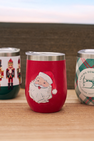 Three festive wine tumblers with different designs on a wooden surface.