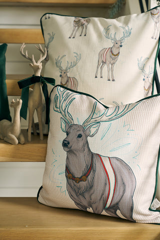 The limited edition Holiday Reindeer Pillow features illustrated reindeer in festive blankets, creating a cozy holiday vibe. Pair it with ceramic reindeer figurines decorated with green ribbon collars for a charming seasonal touch.