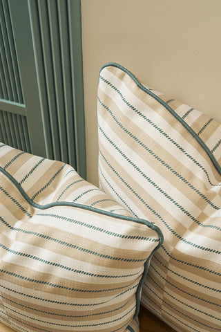 Two Sage King Street Stripes euro pillow covers, featuring beige fabric with diagonal blue and white stripes and blue piping, are set against a light-colored wall and a blue-grey paneled surface.