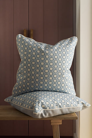 Two Dimensional Dot in Navy Pillows are stacked on a wooden bench in front of a mauve cabinet, with a white wall visible on the right side of the image.