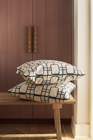 Two Navy Lattice Pillows are stacked on a wooden bench in front of mauve cabinets with long wooden handles, illuminated by sunlight from a nearby window.