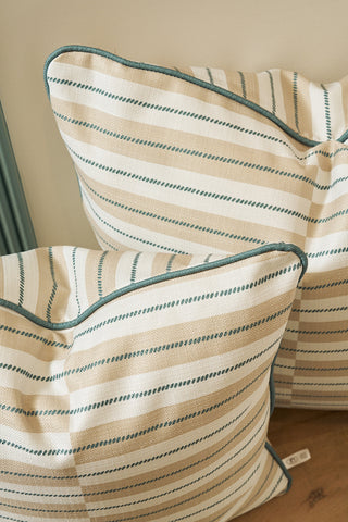 Two Sage King Street Stripes pillows, cream with beige and dark green diagonal stripes plus green piping, are stacked on a wooden surface against a beige wall; each has an oversized cover made in the USA.