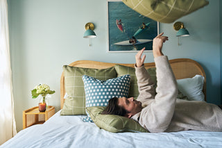 Craig tossing a decorative pillow, while lying on a bed.