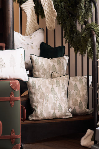 A cozy holiday scene features the Sewing Down South Christmas Tree Farm Pillow on wooden stairs with garland on the railing, white stockings, and a vintage-style suitcase in the foreground.