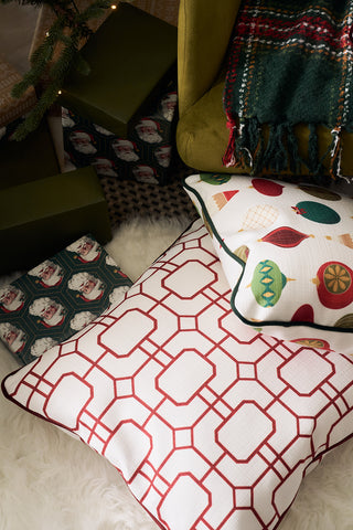 Decorative items like the Red Holiday Lattice Oversized Pillow, a green plaid blanket, and wrapped gifts rest on a fluffy white rug near a Christmas tree, creating a cozy and festive holiday décor scene.