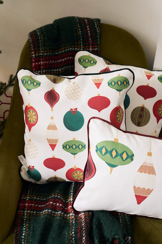 The Classic Ornaments Pillow, with its festive ornament patterns, sits on a green armchair draped in a red and green plaid blanket, creating a cozy holiday atmosphere.