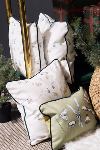 A Ski Resort Pillow with winter sports-themed designs—skis, ski lifts, and gloves—is arranged on a textured rug next to holiday greenery and a wicker basket for cozy vintage ski decor.