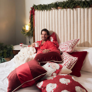 Man sitting on a bed with decorative pillows and Christmas decorations.
