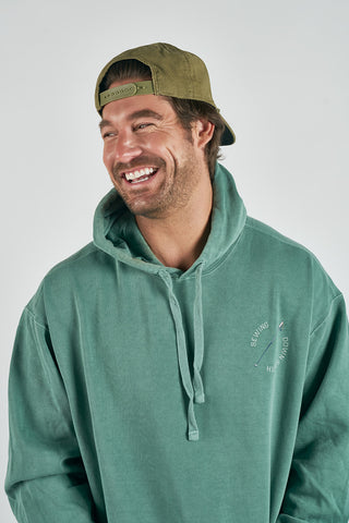 A man in a green Conover Ski Resort Hoodie with a circular logo and an olive green backward cap smiles, channeling mountain-town vibes against a light gray background.