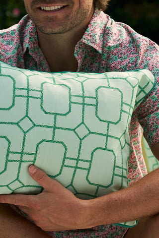A person in a floral shirt holds the Banana Leaves with Green Lattice Lumbar Outdoor Pillow, their face partially visible as they enjoy the fresh air outdoors.
