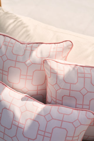 Close-up of three Flamingo with Pink Lattice Lumbar Outdoor Pillows on a light sofa, featuring intersecting lines forming diamond and square patterns. Soft lighting casts shadows that enhance the pastel tones, similar to the allure of a flamingo pillow.