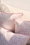 Close-up of three Flamingo with Pink Lattice Lumbar Outdoor Pillows on a light sofa, featuring intersecting lines forming diamond and square patterns. Soft lighting casts shadows that enhance the pastel tones, similar to the allure of a flamingo pillow.