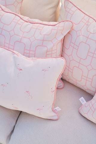 The Pink Lattice Outdoor Pillow collection decorates the couch with pastel pink geometric patterns and flamingos on a white backdrop, crafted from SDS Shield® Outdoor Fabric for a cozy and inviting look.