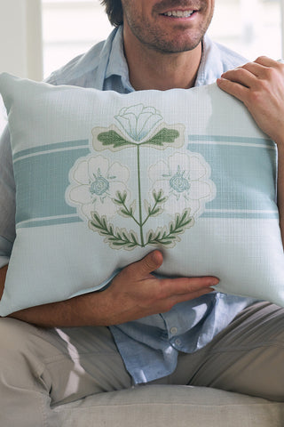 A person wearing a light blue shirt and beige pants, embodying Sewing Down South® style, holds the Bee & Florals Collection: Victorian Floral Stripe Lumbar Pillow. Proudly made in the USA, it features a light blue floral design with embroidered flowers in soft green and white.