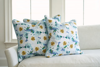 Three decorative Sewing Down South® Bee & Florals Collection: Blossoming Peonies Pillows are arranged on a light-colored sofa. Large windows in the background let in natural light, creating a cozy and bright atmosphere.
