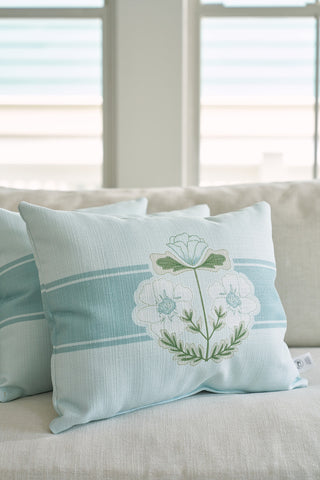 Two light blue Victorian Floral Stripe Lumbar Pillows from the Bee & Florals Collection enhance a cream sofa. Adorned with white and green embroidered flowers by Sewing Down South®, they bring elegance as soft natural light highlights their craftsmanship through nearby windows.