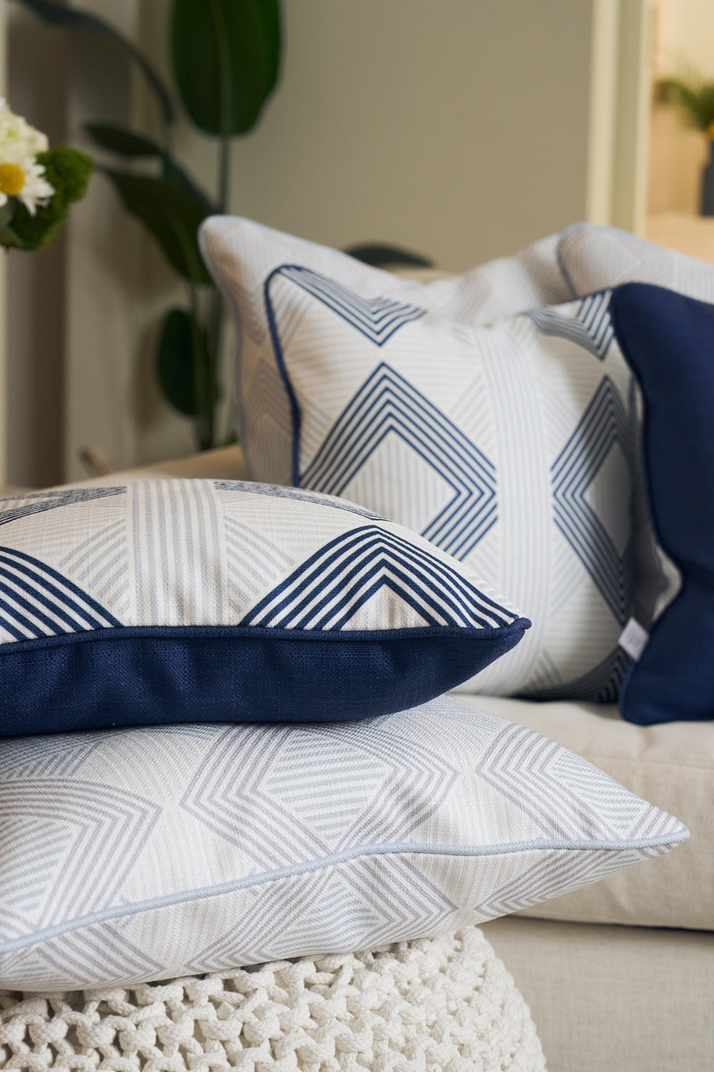 Three decorative pillows, including the Mod Geo Diamond in Navy Pillow, feature geometric blue and white patterns on a light sofa, paired with a green plant and white crocheted throw for stylish Southern-inspired decor.