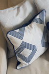 The Mod Geo Diamond in Navy Pillow adds a bold geometric pattern in blue and white to the beige sofa, bringing a touch of Southern-inspired decor with its striking and stylish design.