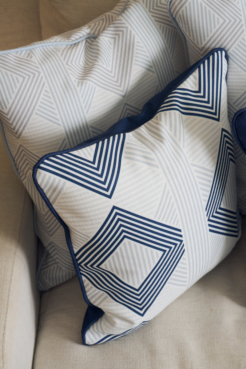 The Mod Geo Diamond in Navy Pillow adds a bold geometric pattern in blue and white to the beige sofa, bringing a touch of Southern-inspired decor with its striking and stylish design.