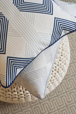 A close-up of the Mod Geo Diamond in Navy Pillow, paired with a navy decorative pillow on a chunky knit pouf. In the background, a subtly geometric rug enhances the perfect Southern aesthetic decor.