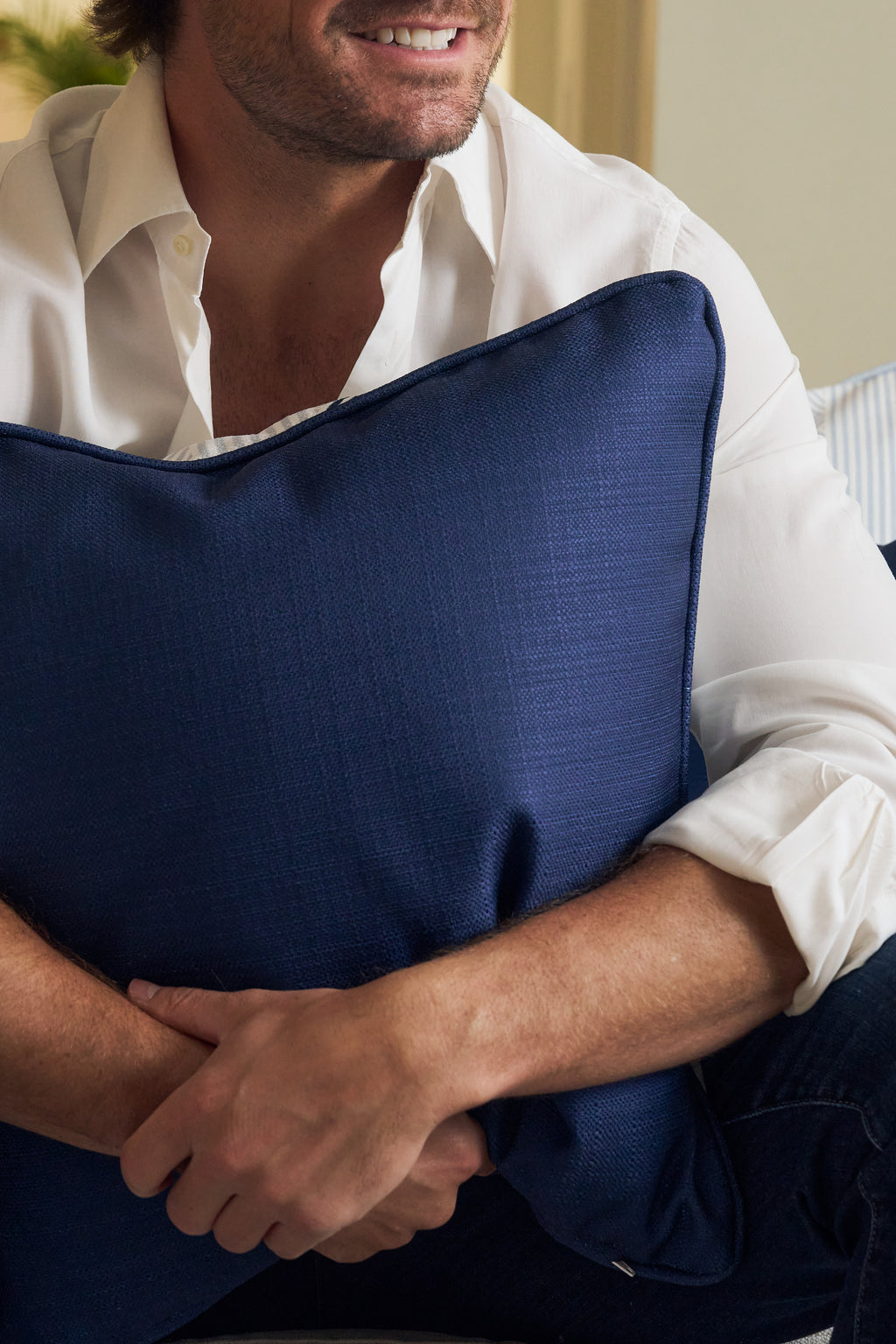 A man in a white shirt sits smiling, hugging a large Mod Geo Diamond in Navy Pillow with his arms wrapped around it. Only his mouth and chin are visible—ideal for fans of modern decor.