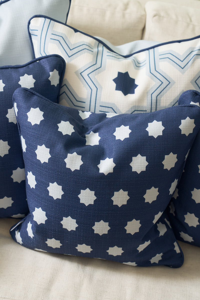 Three decorative pillows with blue and white star patterns rest on a light-colored couch. The front Mod Stars Pillow showcases its repeating star motif, complemented by a bold geometric design pillow behind it.