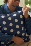A man in a blue button-up shirt smiles while hugging the Mod Stars Pillow, which showcases a navy-blue and white geometric star pattern.