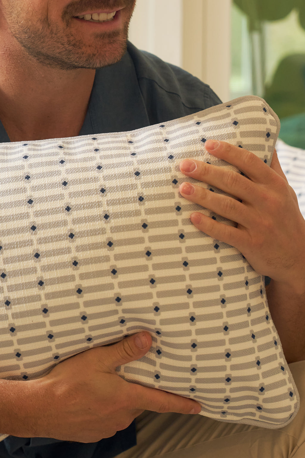 A person in a blue shirt holds the Mod Mini Crossing Tiles Lumbar Pillow, a rectangular accent pillow with blue dotted patterns and stripes, showcasing this stylish Southern-inspired decor.