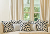 A beige sofa with five decorative pillows, including three Oversized Modern Polka Dots Pillows and two plain light-colored ones, sits by large windows with cream curtains. Greenery outside brings a fresh feel to this inviting southern decor.