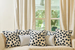 A beige sofa with five decorative pillows, including three Oversized Modern Polka Dots Pillows and two plain light-colored ones, sits by large windows with cream curtains. Greenery outside brings a fresh feel to this inviting southern decor.
