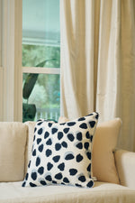 A cream-colored sofa with the Oversized Modern Polka Dots Pillow, featuring a hand-painted pattern, sits by a window with sheer beige curtains and views of lush greenery, adding a hint of Southern decor.