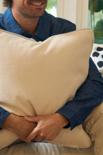 A person in a blue shirt sits on a couch, smiling and hugging the Oversized Modern Polka Dots Pillow in beige. Only the lower half of their face is visible, adding a cozy hint of southern decor to the scene.