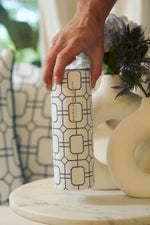 A hand holds the Blue Lattice 20oz Tumbler from Sewing Down South, a stainless steel insulated tumbler with a blue geometric pattern and EVINO & SMITH label, resting on marble next to a white vase with flowers.