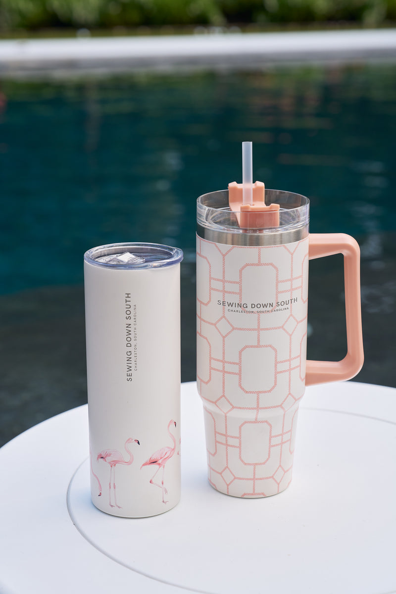 Two insulated tumblers sit on a white table by the pool: one white with pink flamingos, the other a Pink Lattice 30oz Tumbler with handle. Both have Sewing Down South labels and a no-sweat exterior for your favorite beverages.