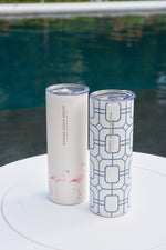 Two tall stainless steel tumblers with lids sit poolside. One 20oz cup is cream with pink flamingos, the other is the Blue Lattice 20oz Tumbler, white with a blue geometric pattern. Both have a no sweat exterior and SEWING DOWN SOUTH label.