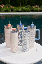 Five Blue Lattice 20oz stainless steel tumblers with straws and no-sweat exterior are arranged on a white round table beside a swimming pool, with greenery and flowers in the background.
