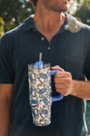 A man in a dark blue polo shirt holds the Crab Craze 30oz Tumbler, a stainless steel insulated cup with a blue handle, blue crab design, plastic straw, and no-sweat exterior—ideal for enjoying drinks outdoors.